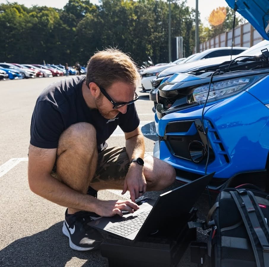 Hands-on laptop calibration beside a blue Honda Civic