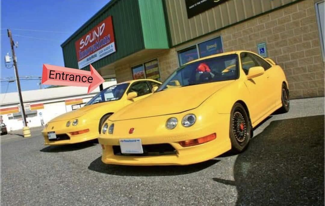 IMW storefront: red Entrance arrow points to the covered glass door beside the yellow cars